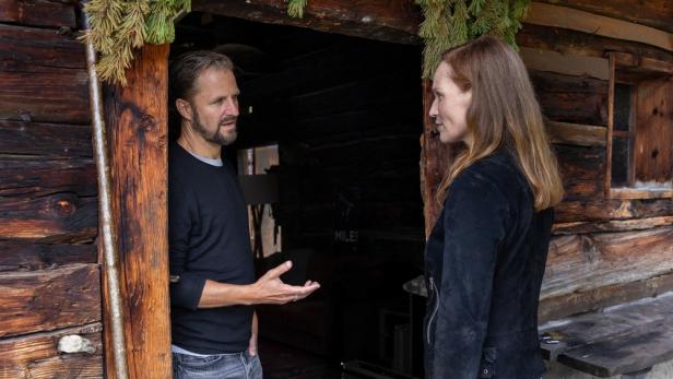 Ein Mann und eine Frau unterhalten sich vor dem Eingang einer rustikalen Holzhütte.