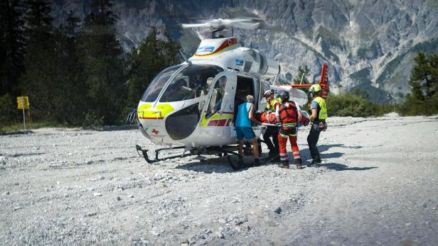 Rettungskräfte laden eine verletzte Person in einem Gebirge in einen Rettungshubschrauber des ÖAMTC.