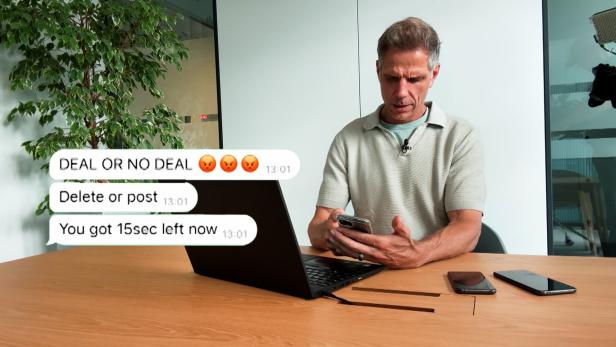 Mann am Tisch schaut angespannt aufs Smartphone, neben dem Laptop stehen Chatblasen mit Drohungen.