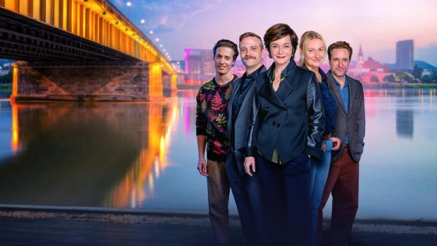 Fünf Personen stehen vor einer beleuchteten Brücke über die Linzer Donau bei Dämmerung.