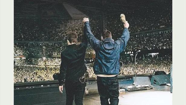 Oasis-Mitglieder auf der Bühne vor jubelndem Stadionpublikum, darüber der Titel „Don’t Look Back in Anger“.