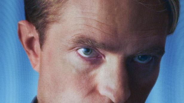 Robert Pattinson blickt ernst auf dem Filmplakat zu „Primetime“ von Regisseur Lance Oppenheim vor einem blauen Hintergrund.