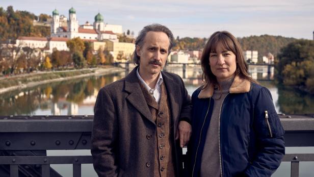 Ein Mann und eine Frau stehen auf einer Brücke vor der Kulisse der Passauer Altstadt mit dem Dom St. Stephan im Hintergrund.