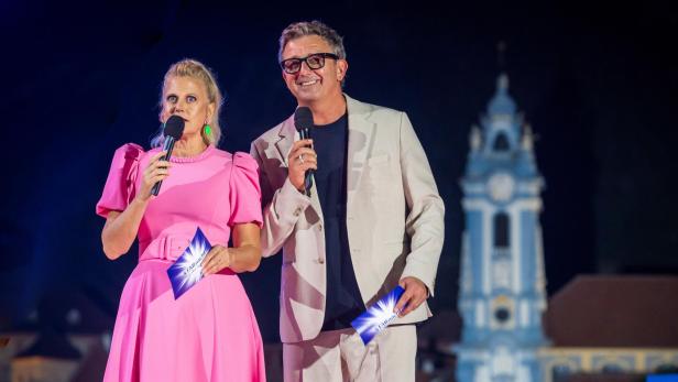 Barbara Schöneberger und Hans Sigl moderieren mit Mikrofonen vor einer beleuchteten Kirche bei der Starnacht.