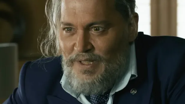Johnny Depp mit grauem Bart und zurückgekämmtem Haar trägt ein blaues Sakko mit hellblauem Hemd und gepunkteter Krawatte.