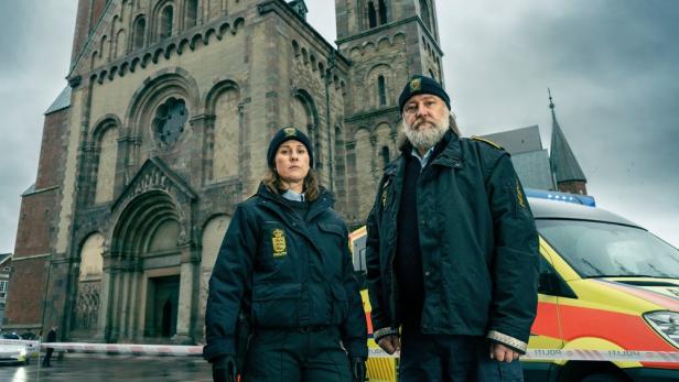 Zwei Polizisten stehen vor einer Kathedrale neben einem Einsatzfahrzeug.