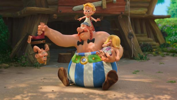 Obelix sitzt vor einer Hütte und hält spielerisch drei Kinder, während eines auf seinem Kopf und zwei in seinen Armen sind.