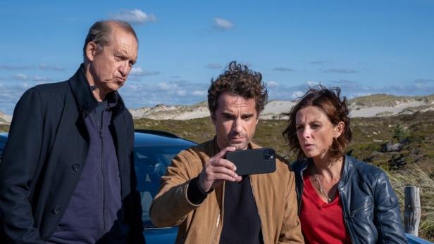 Drei Personen stehen draußen vor einem Auto und schauen gemeinsam auf ein Smartphone.