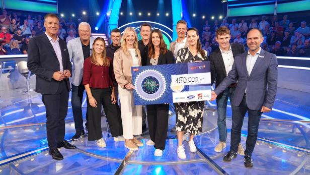 Eine Gruppe von Personen steht auf einer Fernsehbühne und hält gemeinsam einen großen Scheck über 150.000 Euro in die Höhe.