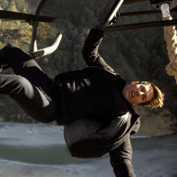 Tom Cruise hängt an einem Hubschrauber über einer Landschaft.