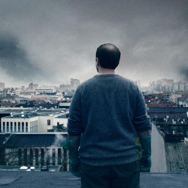 Ein Mann steht auf einem Dach und blickt auf die Skyline von Berlin mit Rauchwolken.