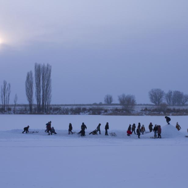 Eine Gruppe von Menschen genießt einen Wintertag mit Schlittenfahren auf einer schneebedeckten Fläche.