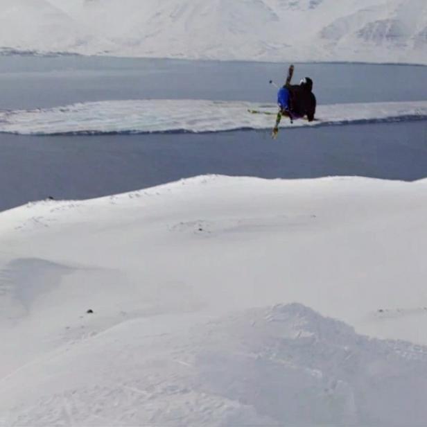 Ein Skifahrer springt vor einer verschneiten Berglandschaft in der Luft.
