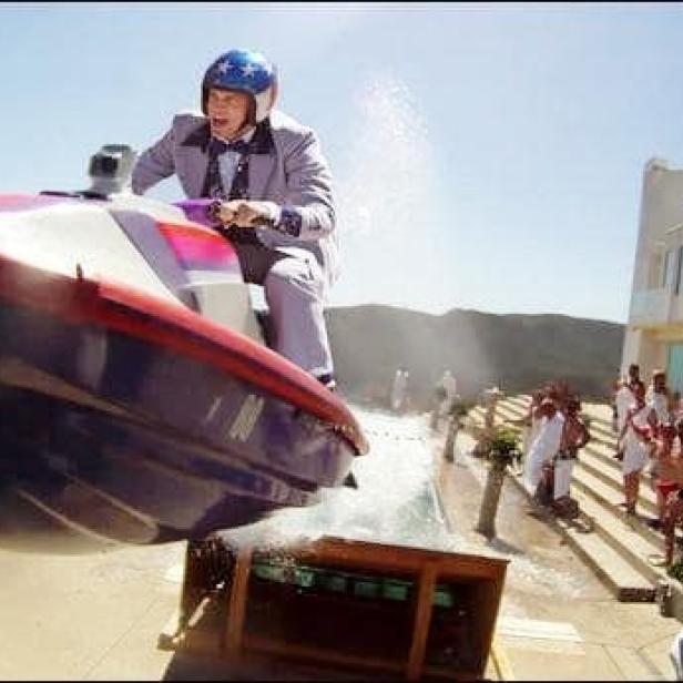Ein Mann im Anzug und Helm springt mit einem Jetboot über einen Pool.