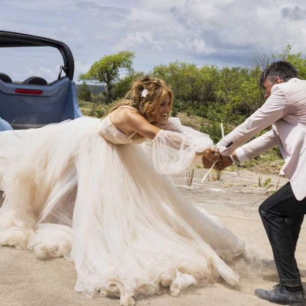 Jennifer Lopez in einem Hochzeitskleid wird von einem Mann weggezogen.