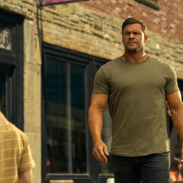 Jack Reacher geht an einem Jungen vorbei eine Straße entlang.