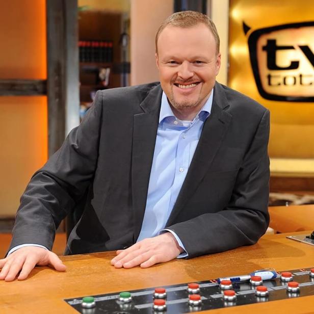 Stefan Raab sitzt lächelnd am Schreibtisch von „TV total“.