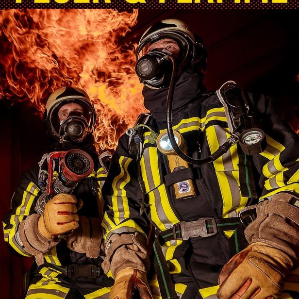 Zwei Feuerwehrleute in Schutzkleidung stehen vor einem Feuer.