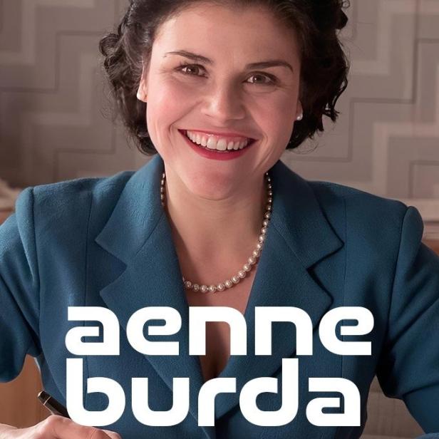 Aenne Burda lächelt, während sie mit einem Füller schreibt.