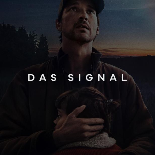 Ein Mann umarmt ein Kind vor dem Hintergrund des Posters für „Das Signal“.