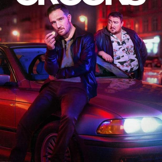 Zwei Männer posieren auf der Motorhaube eines Autos für die Netflix-Serie „Crooks“.