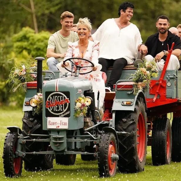 Inka Bause lenkt Traktor mit Anhänger, auf dem Bauern sitzen