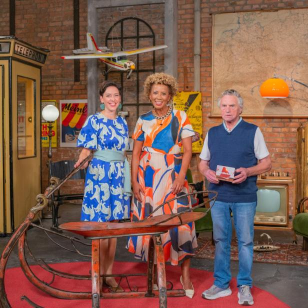 Arabella Kiesbauer steht im Studio vor einem historischen Gasslschlitten