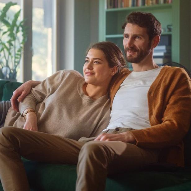 Aneinandergekuscheltes Pärchen daheim auf der Couch beim Streamen