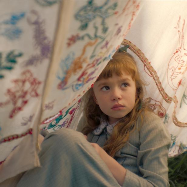 Mädchen sitzt unter einer bunten Decke