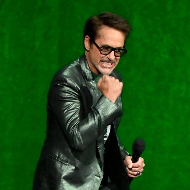 Robert Downey Jr. mit geballter Faust un Mikro in der andern Hand vor grünem Hintergrund