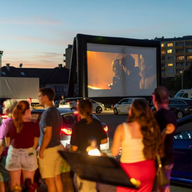 Abendliche Sommerkino-Locaton mit Publikum, Autos und Leinwand im Hintergrund