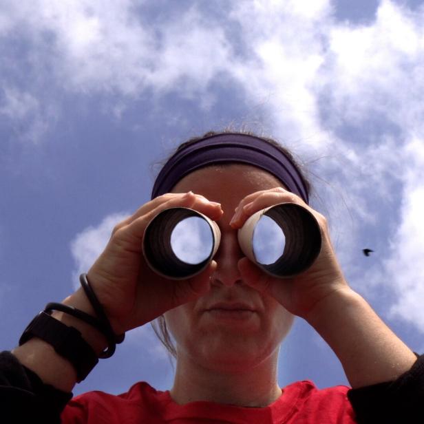 Figur mit Fernglas vor Augen, in dem sich der Himmel spiegelt