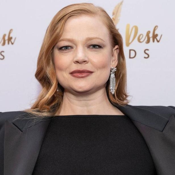 Sarah Snook mit Blazer und Ohrringen vor dem Hintergrund der Drama Desk Awards.