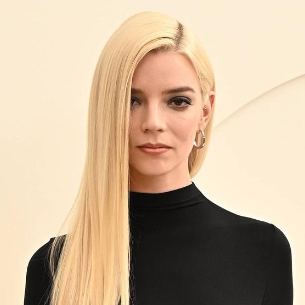 Anya Taylor-Joy mit langem, blondem Haar und schwarzem Oberteil vor einem hellen Hintergrund.
