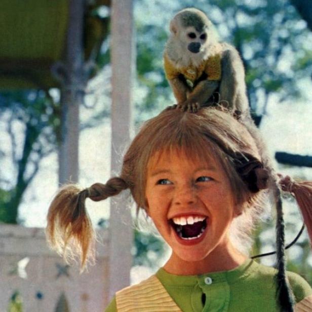 Pippi Langstrumpf lacht fröhlich mit ihrem Totenkopfäffchen Herr Nilsson auf dem Kopf.