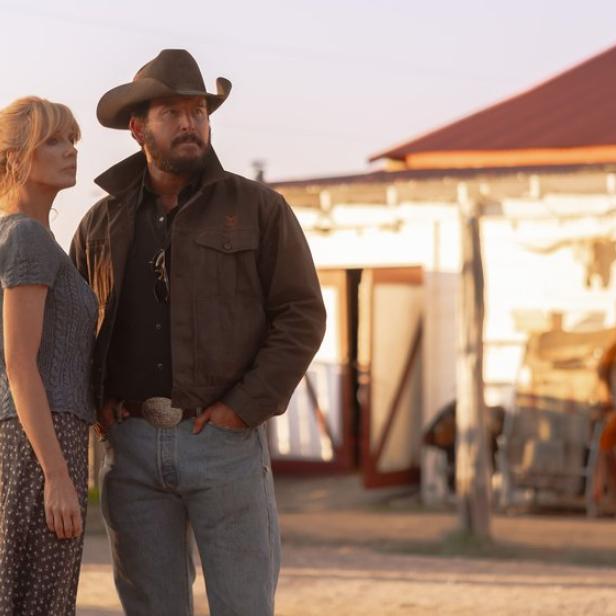 Beth Dutton und Rip Wheeler stehen vor einer Ranch im warmen Licht der Abendsonne.
