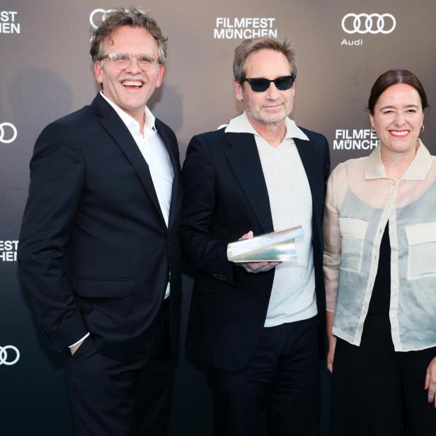 David Duchovny steht mit zwei Personen vor einer Sponsorenwand des Filmfest München.
