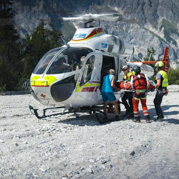 Rettungskräfte laden eine verletzte Person in einem Gebirge in einen Rettungshubschrauber des ÖAMTC.