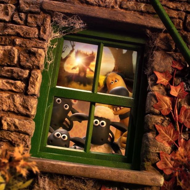 Shaun das Schaf und seine Freunde schauen neugierig aus einem Fenster eines alten Steinhauses auf eine sonnige Landschaft.