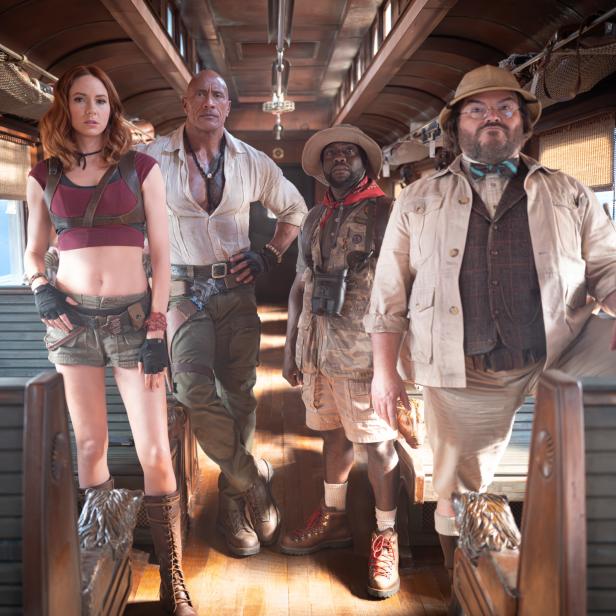 Karen Gillan, Dwayne Johnson, Kevin Hart und Jack Black stehen in Abenteurerkleidung in einem historischen Zugwaggon.