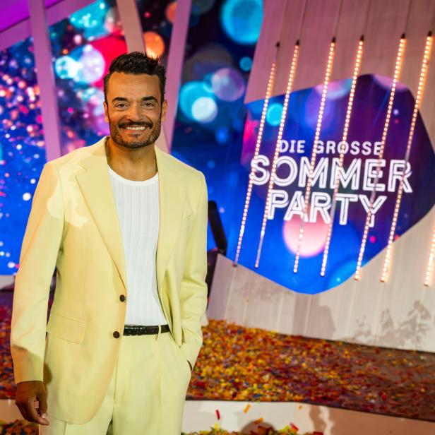 Giovanni Zarrella lächelt in einem hellgelben Anzug vor dem Bühnenhintergrund der Sendung „Die große Sommerparty“.