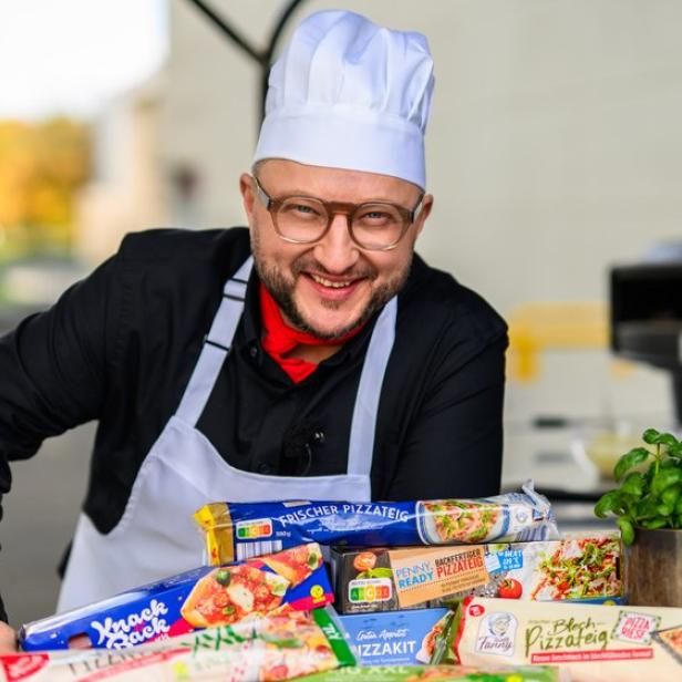 Ein lächelnder Koch mit weißer Mütze präsentiert verschiedene Packungen Pizzateig vor einem Pizzaofen.