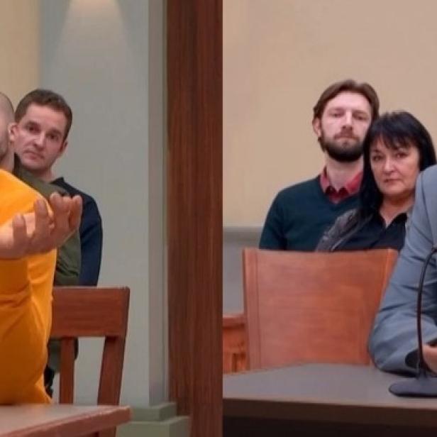 Zwei Männer sitzen nacheinander an einem Tisch vor einem Mikrofon, während im Hintergrund ein Publikum in einem Studio zuschaut.