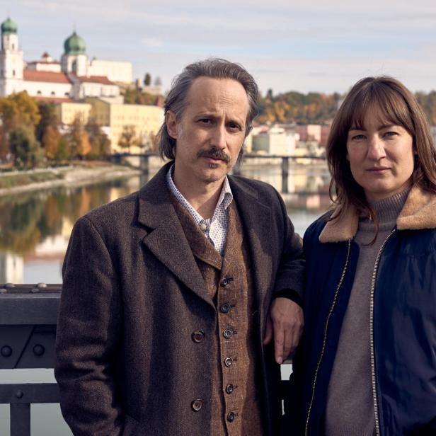 Ein Mann und eine Frau stehen auf einer Brücke vor der Kulisse der Passauer Altstadt mit dem Dom St. Stephan im Hintergrund.