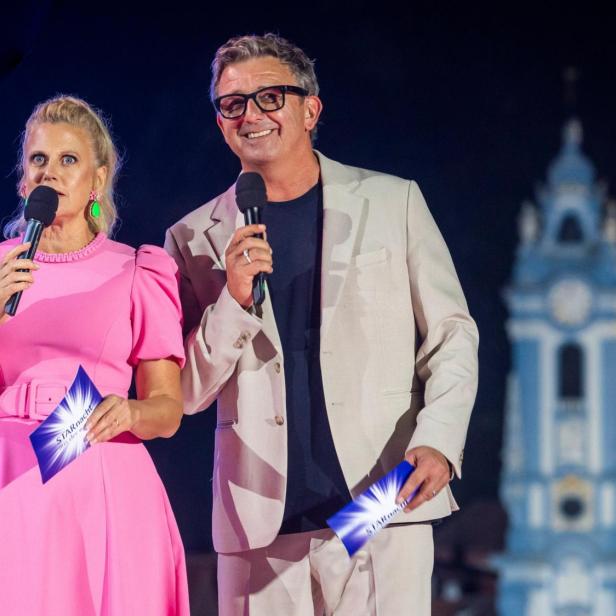 Barbara Schöneberger und Hans Sigl moderieren mit Mikrofonen vor einer beleuchteten Kirche bei der Starnacht.