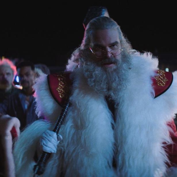 Ein als Weihnachtsmann gekleideter Mann mit Axt geht entschlossen durch die Nacht, gefolgt von einer Frau und weiteren Personen.