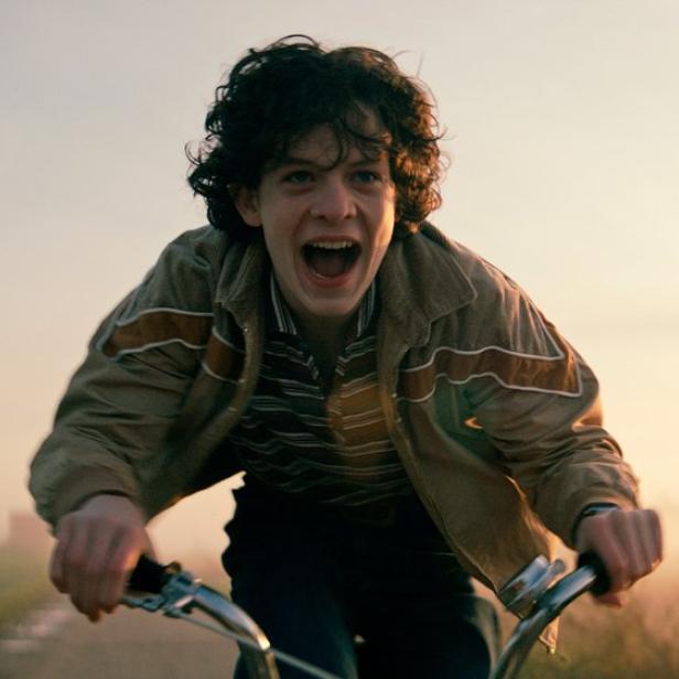 Junger Mann fährt mit dem Fahrrad und schreit in die Kamera bei Sonnenuntergang.