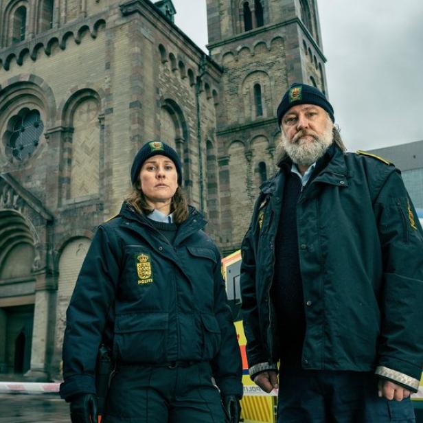 Zwei Polizisten stehen vor einer Kathedrale neben einem Einsatzfahrzeug.