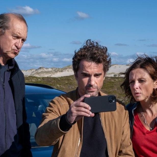 Drei Personen stehen draußen vor einem Auto und schauen gemeinsam auf ein Smartphone.