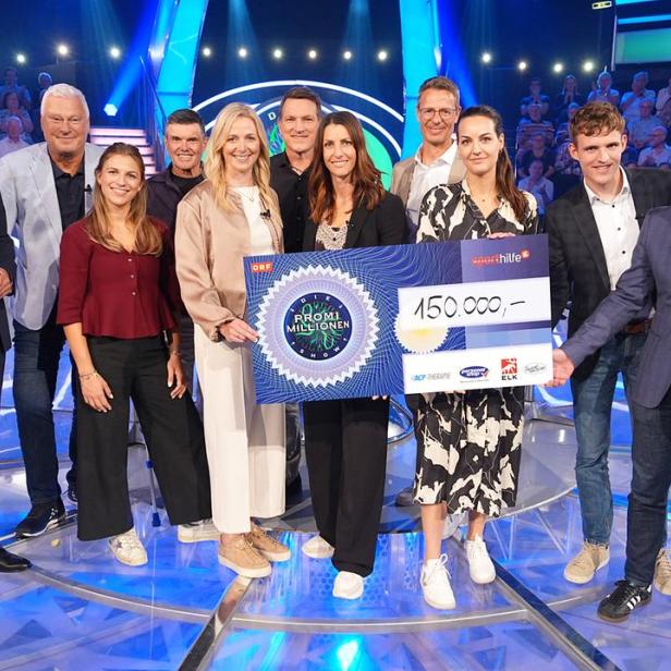Eine Gruppe von Personen steht auf einer Fernsehbühne und hält gemeinsam einen großen Scheck über 150.000 Euro in die Höhe.